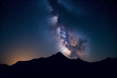 Éjszakai égbolt csillagokkal tele, felette egy sötét hegy sziluettje.